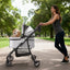 Gray foldable pet stroller with a small dog on a park path