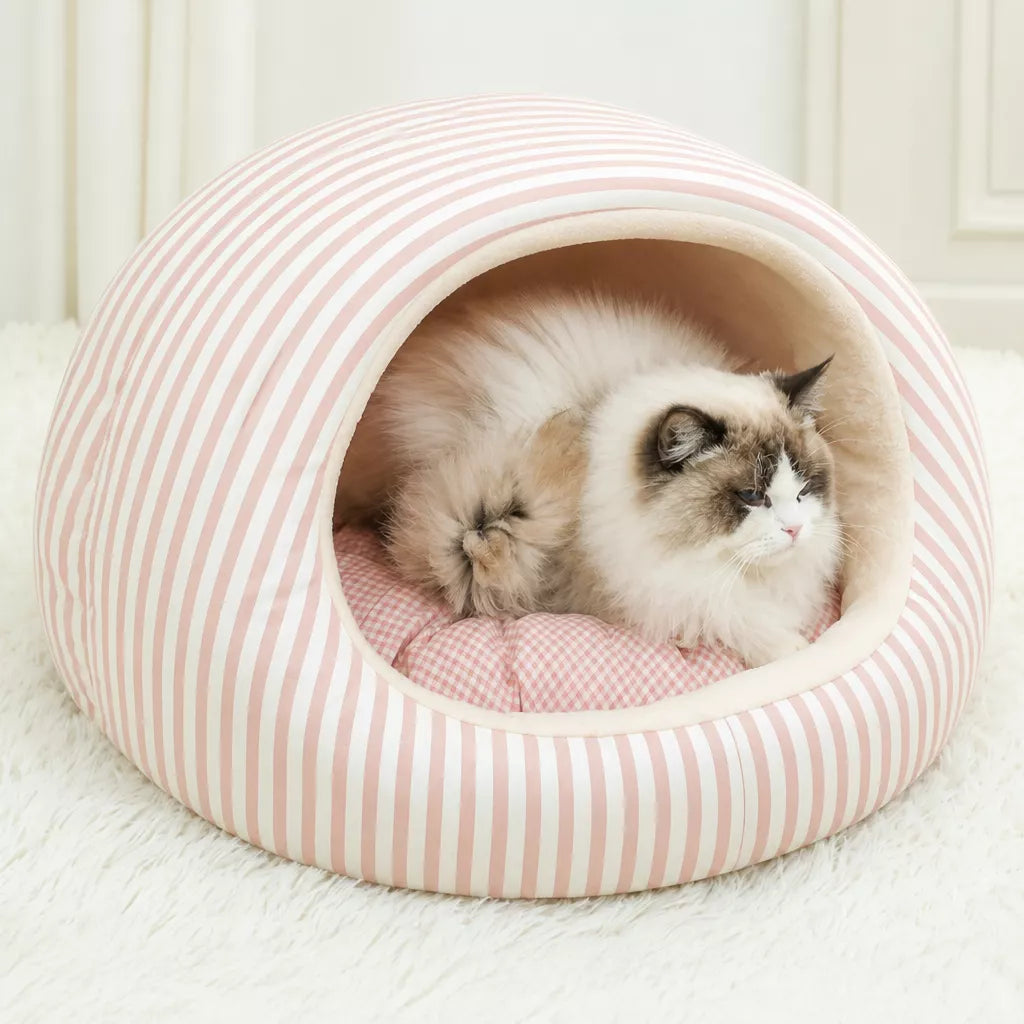 Cat resting inside a pink striped pet cave bed