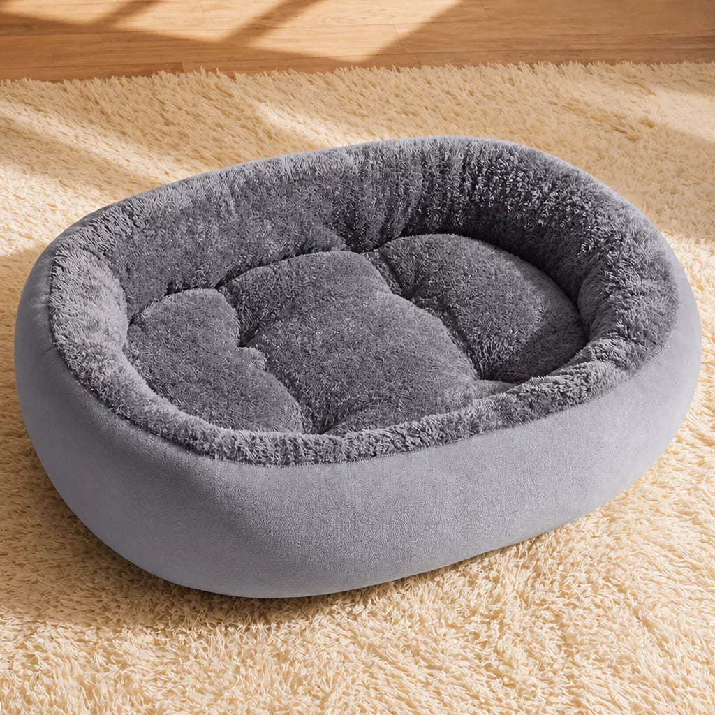 Gray oval fleece pet bed beside a rug