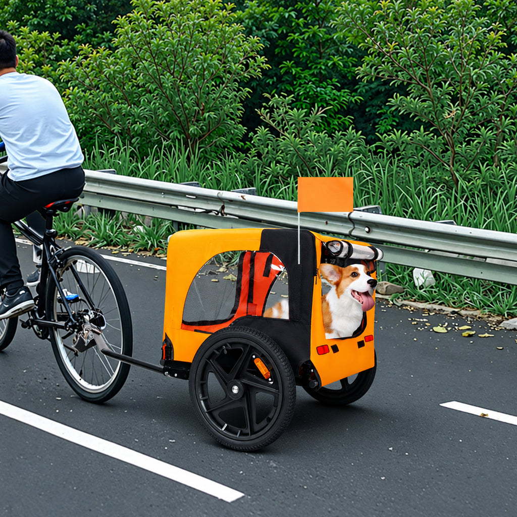 Black and orange pet bike trailer with a corgi attached to a bicycle on a roadside path
