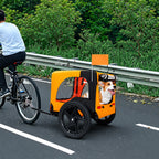 Black and orange pet bike trailer with a corgi attached to a bicycle on a roadside path